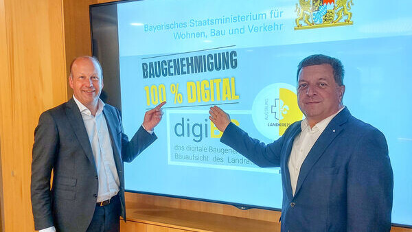 Landrat Martin Sailer (links) und Staatsminister Christian Bernreiter freuen sich über die erste digital versendete Baugenehmigung in Bayern. 